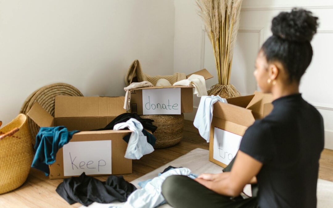 A woman sitting on the floor organizing her belongings into labeled boxes 'keep,' 'donate,' and 'throw away' as part of organizing your space after moving.